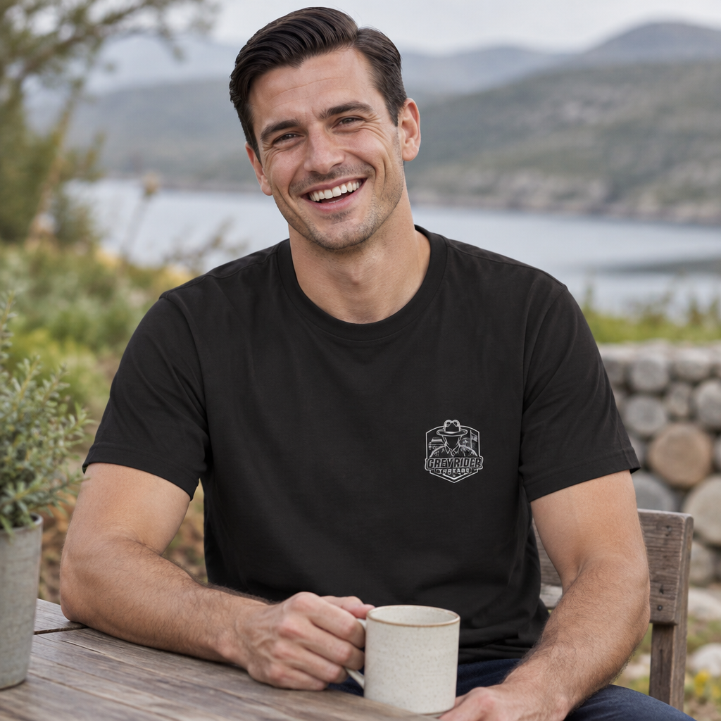 Smiling man in a black Weathered Compass tee with the GreyRider Threads left-chest logo, holding a mug